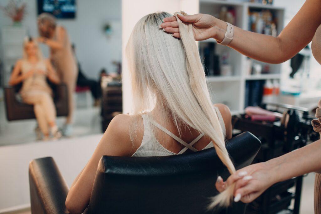 Friseurfrau macht Haarverlängerungen für junge Frau mit blonden Haaren im Schönheitssalon. Professioneller Haarverlängerungssalon