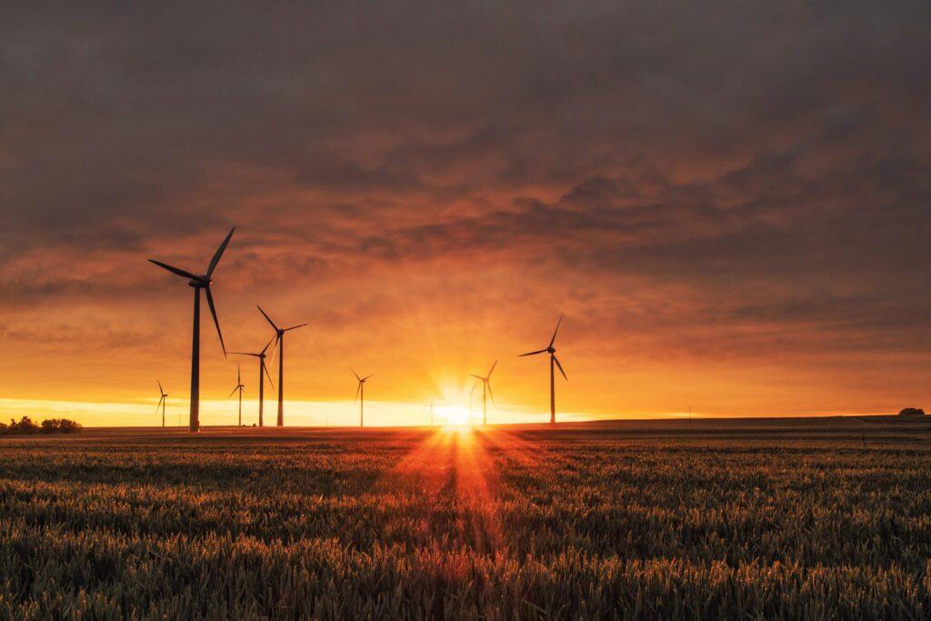 Windräder auf einem Feld bei Sonnenuntergang, die die Bedeutung von erneuerbaren Energien wie Windkraft und Photovoltaikanlagen in Karlsruhe für eine nachhaltige Energiezukunft symbolisieren.