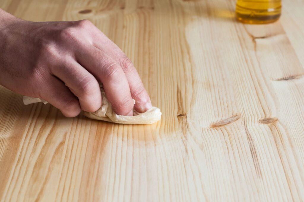 Hand ölt einen Esstisch aus Massivholz, um die Oberfläche zu schützen und die natürliche Maserung des Holzes zu bewahren.