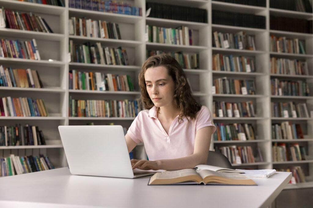 Junge Frau arbeitet in der Bibliothek an ihrer Dissertation – Sinnbild für Fokus und Selbstverantwortung beim Doktorarbeit schreiben lassen